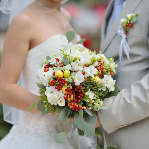 Bride and groom are holding wedding flower bouquet of white roses in summer park on walking. Time for photos