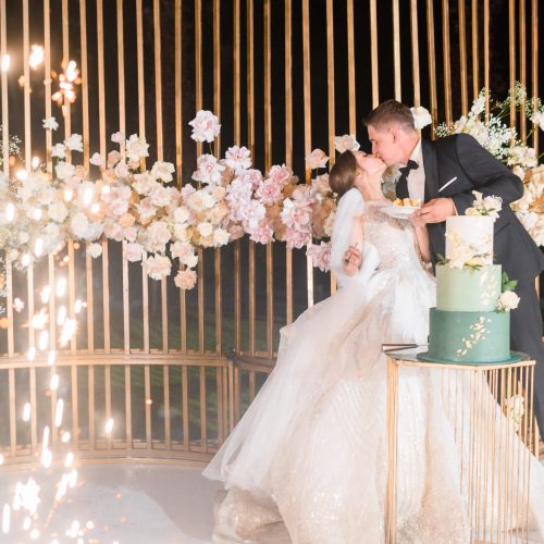 side-view-happy-bride-groom-which-eating-wedding-cake-kissing-each-other-while-standing-background-beautiful-wedding-arch-which-decorated-by-metal-roses-during-evening-ceremony